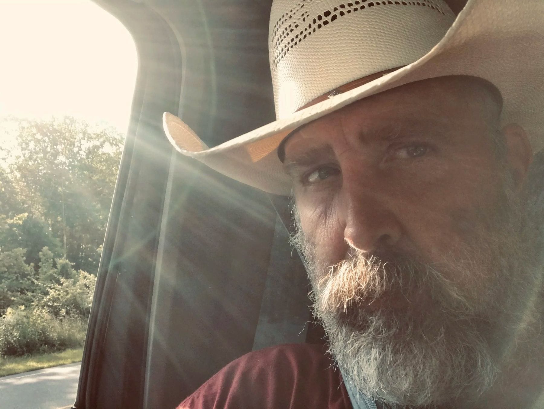 Nute Nicholson in a straw cowboy hat, sunlight through the truck window