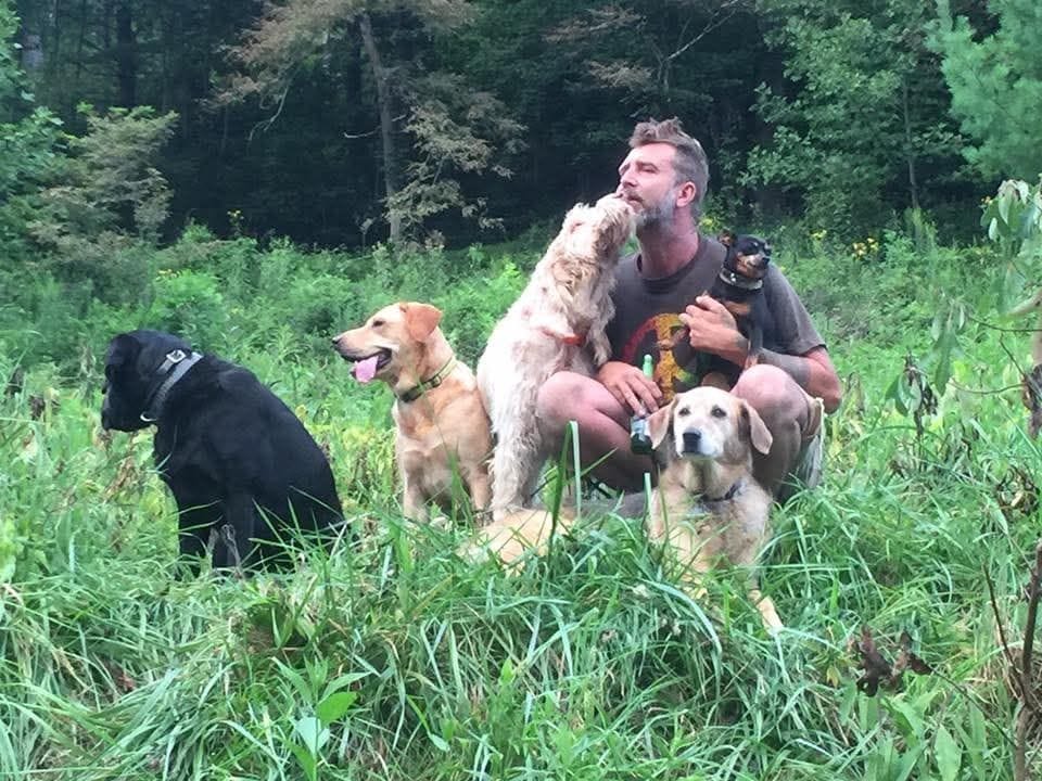Nute kneeling in tall grass with four dogs